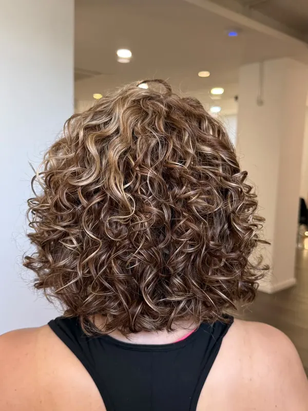 O mesmo cabelo com cachos definidos e mechas iluminadas, depois do atendimento